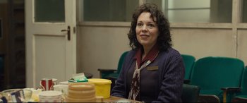 Movie still from “Empire of Light” (2022), directed by Sam Mendes – A woman sitting in front of a table with yellow cups on top of it; Medium shot, Over the shoulder angle