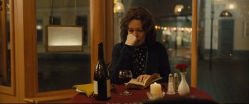 Movie still from “Empire of Light” (2022), directed by Sam Mendes – A woman sitting at a table reading a book; Medium shot, Over the shoulder angle