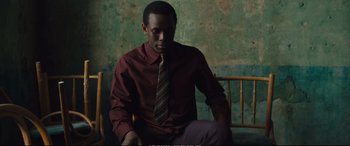 Movie still from “Empire of Light” (2022), directed by Sam Mendes – A man sitting in a chair wearing a tie; Medium shot, High angle