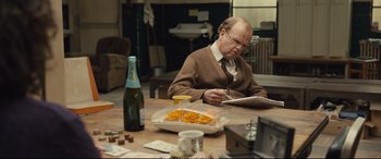 Movie still from “Empire of Light” (2022), directed by Sam Mendes – A man sitting at a wooden table with a bottle of wine; Medium shot, Over the shoulder angle