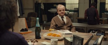 Movie still from “Empire of Light” (2022), directed by Sam Mendes – An older man sitting at a table in front of some food; Medium shot, Over the shoulder angle