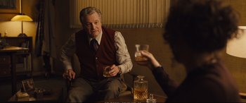 Movie still from “Empire of Light” (2022), directed by Sam Mendes – A man sitting at a table with a glass of whiskey; Medium shot, Over the shoulder angle