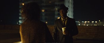 Movie still from “Empire of Light” (2022), directed by Sam Mendes – A man in a suit and hat holding a cup; Medium shot, Over the shoulder angle