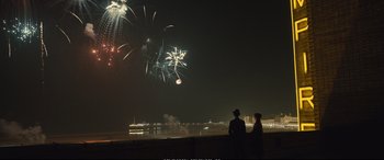 Movie still from “Empire of Light” (2022), directed by Sam Mendes – Two people looking at fireworks over a body of water at night; Extreme Wide shot, Over the shoulder angle