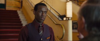 Movie still from “Empire of Light” (2022), directed by Sam Mendes – A man in a vest and tie standing in front of a staircase; Close Up shot, Over the shoulder angle