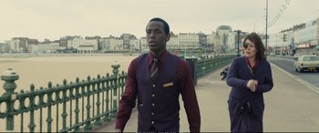 Movie still from “Empire of Light” (2022), directed by Sam Mendes – A man in a vest and tie standing in front of a fence; Medium shot, Over the shoulder angle