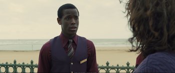 Movie still from “Empire of Light” (2022), directed by Sam Mendes – A man wearing a purple vest and a striped tie standing in front of the ocean; Close Up shot, Over the shoulder angle
