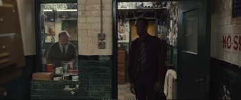 Movie still from “Empire of Light” (2022), directed by Sam Mendes – A man standing in front of a brick wall in a room; Medium shot, Over the shoulder angle