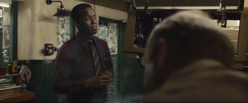 Movie still from “Empire of Light” (2022), directed by Sam Mendes – A man wearing a suit and tie holding a cup; Medium shot, Over the shoulder angle