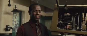 Movie still from “Empire of Light” (2022), directed by Sam Mendes – A man wearing a suit and tie smiling for the camera; Close Up shot, Low angle