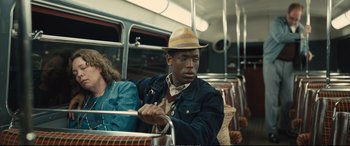Movie still from “Empire of Light” (2022), directed by Sam Mendes – A man riding on a bus wearing a hat; Medium shot, Over the shoulder angle