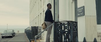 Movie still from “Empire of Light” (2022), directed by Sam Mendes – A man standing on the side of the street holding a bag; Wide shot, Low angle