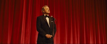 Movie still from “Empire of Light” (2022), directed by Sam Mendes – A man in a tuxedo standing in front of a microphone on a stage; Medium shot, Low angle