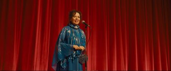 Movie still from “Empire of Light” (2022), directed by Sam Mendes – A woman standing on a stage holding a microphone; Medium shot, Over the shoulder angle
