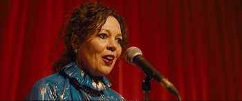 Movie still from “Empire of Light” (2022), directed by Sam Mendes – A woman is speaking into a microphone on a stage; Close Up shot, Over the shoulder angle