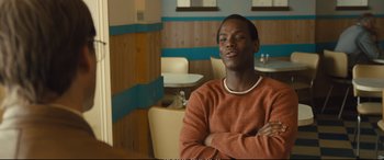 Movie still from “Empire of Light” (2022), directed by Sam Mendes – A man sitting at a table with his arms crossed; Medium shot, Over the shoulder angle