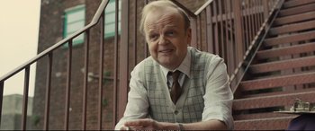 Movie still from “Empire of Light” (2022), directed by Sam Mendes – An older man in a vest and tie is smiling for the camera; Close Up shot, Over the shoulder angle