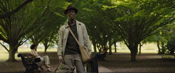 Movie still from “Empire of Light” (2022), directed by Sam Mendes – A man in a hat is standing in a park with a bag; Medium shot, Low angle