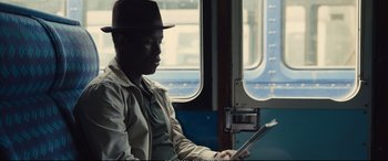 Movie still from “Empire of Light” (2022), directed by Sam Mendes – A man sitting on a train looking at a tablet; Medium shot, Over the shoulder angle