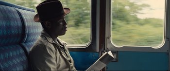 Movie still from “Empire of Light” (2022), directed by Sam Mendes – A person sitting on a train holding a book; Medium shot, Over the shoulder angle