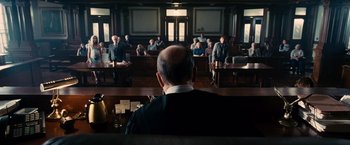 Movie still from “The Judge” (2014), directed by David Dobkin – A man sitting in front of a group of people in a court room; Wide shot, High angle