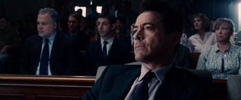 Movie still from “The Judge” (2014), directed by David Dobkin – A man in a suit sitting in front of other men; Close Up shot, Over the shoulder angle