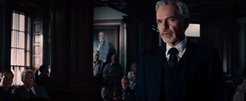 Movie still from “The Judge” (2014), directed by David Dobkin – A man in a suit and tie in front of a group of people; Medium shot, Low angle