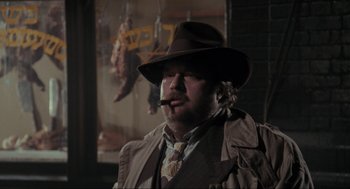 Movie still from “Batman” (1989), directed by Tim Burton – A man wearing a hat and smoking a pipe; Close Up shot, Over the shoulder angle