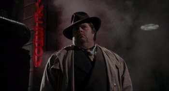 Movie still from “Batman” (1989), directed by Tim Burton – A man wearing a hat and a trench coat standing in front of a building; Medium shot, Low angle