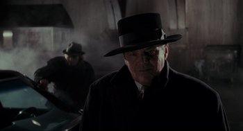 Movie still from “Batman” (1989), directed by Tim Burton – An older man wearing a black hat and a black coat; Close Up shot, Low angle