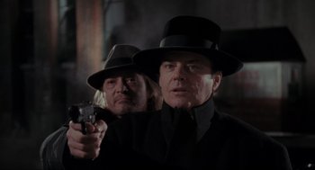 Movie still from “Batman” (1989), directed by Tim Burton – A man in a hat holding a gun next to another man in a hat; Close Up shot, Over the shoulder angle