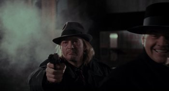Movie still from “Batman” (1989), directed by Tim Burton – A man in a hat is holding a gun; Close Up shot, Over the shoulder angle