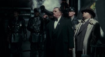Movie still from “Batman” (1989), directed by Tim Burton – An older man in a suit and tie holding a megaphone; Medium shot, Low angle