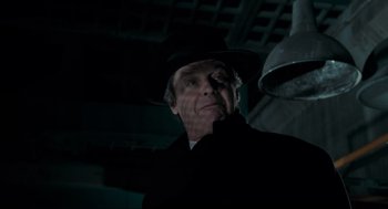 Movie still from “Batman” (1989), directed by Tim Burton – An older man wearing a black hat and a black coat; Close Up shot, Low angle