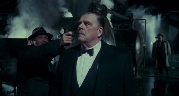 Movie still from “Batman” (1989), directed by Tim Burton – An older man in a tuxedo holding a cell phone up to his ear; Medium shot, Low angle