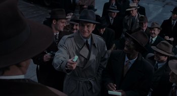 Movie still from “Batman” (1989), directed by Tim Burton – A man in a trench coat holding a cell phone in front of a group of men; Medium shot, High angle