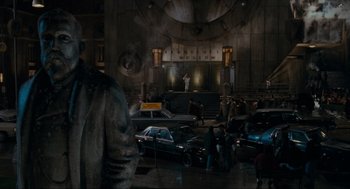 Movie still from “Batman” (1989), directed by Tim Burton – A group of people standing in a room with cars; Wide shot, Low angle