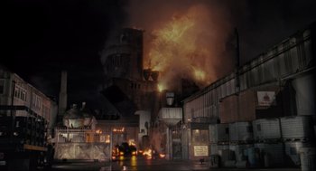 Movie still from “Batman” (1989), directed by Tim Burton – An industrial building on fire at night with smoke billowing from it; Extreme Wide shot, Low angle