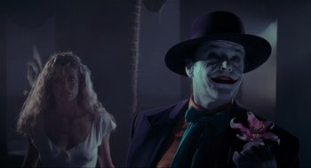 Movie still from “Batman” (1989), directed by Tim Burton – A man with a joker mask and a woman in the background; Medium shot, Over the shoulder angle