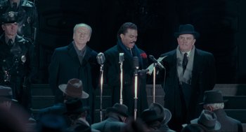 Movie still from “Batman” (1989), directed by Tim Burton – A group of men standing next to each other on a stage with microphones and microphones; Medium shot, Low angle