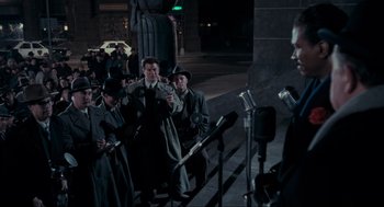 Movie still from “Batman” (1989), directed by Tim Burton – A group of men standing next to each other on a sidewalk; Wide shot, Over the shoulder angle