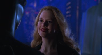 Movie still from “Batman Forever” (1995), directed by Joel Schumacher – A woman with blonde hair and red lipstick smiling for the camera; Close Up shot, Over the shoulder angle