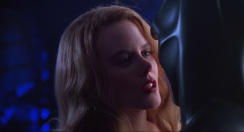 Movie still from “Batman Forever” (1995), directed by Joel Schumacher – A woman with blonde long hair and red lipstick looking into a mirror; Close Up shot, Over the shoulder angle