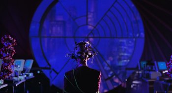 Movie still from “Batman Forever” (1995), directed by Joel Schumacher – A woman with a flower in her hair sitting in front of a window; Close Up shot, Over the shoulder angle