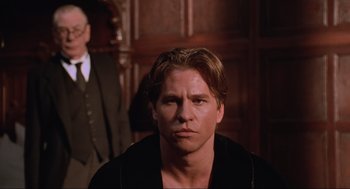 Movie still from “Batman Forever” (1995), directed by Joel Schumacher – A person wearing a suit and tie; Medium shot, Over the shoulder angle