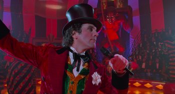 Movie still from “Batman Forever” (1995), directed by Joel Schumacher – A man wearing a top hat and holding a microphone in his hand; Medium shot, Low angle