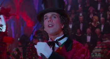 Movie still from “Batman Forever” (1995), directed by Joel Schumacher – A man wearing a top hat and holding a microphone in his hand; Close Up shot, Low angle