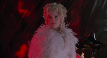 Movie still from “Batman Forever” (1995), directed by Joel Schumacher – A woman in a white dress and a white feather boa; Medium shot, Low angle