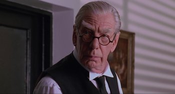 Movie still from “Batman Forever” (1995), directed by Joel Schumacher – An older man wearing glasses and a tie; Close Up shot, Low angle