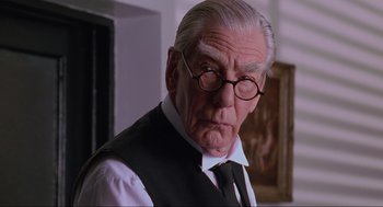 Movie still from “Batman Forever” (1995), directed by Joel Schumacher – An older man wearing glasses and a tie; Close Up shot, Low angle
